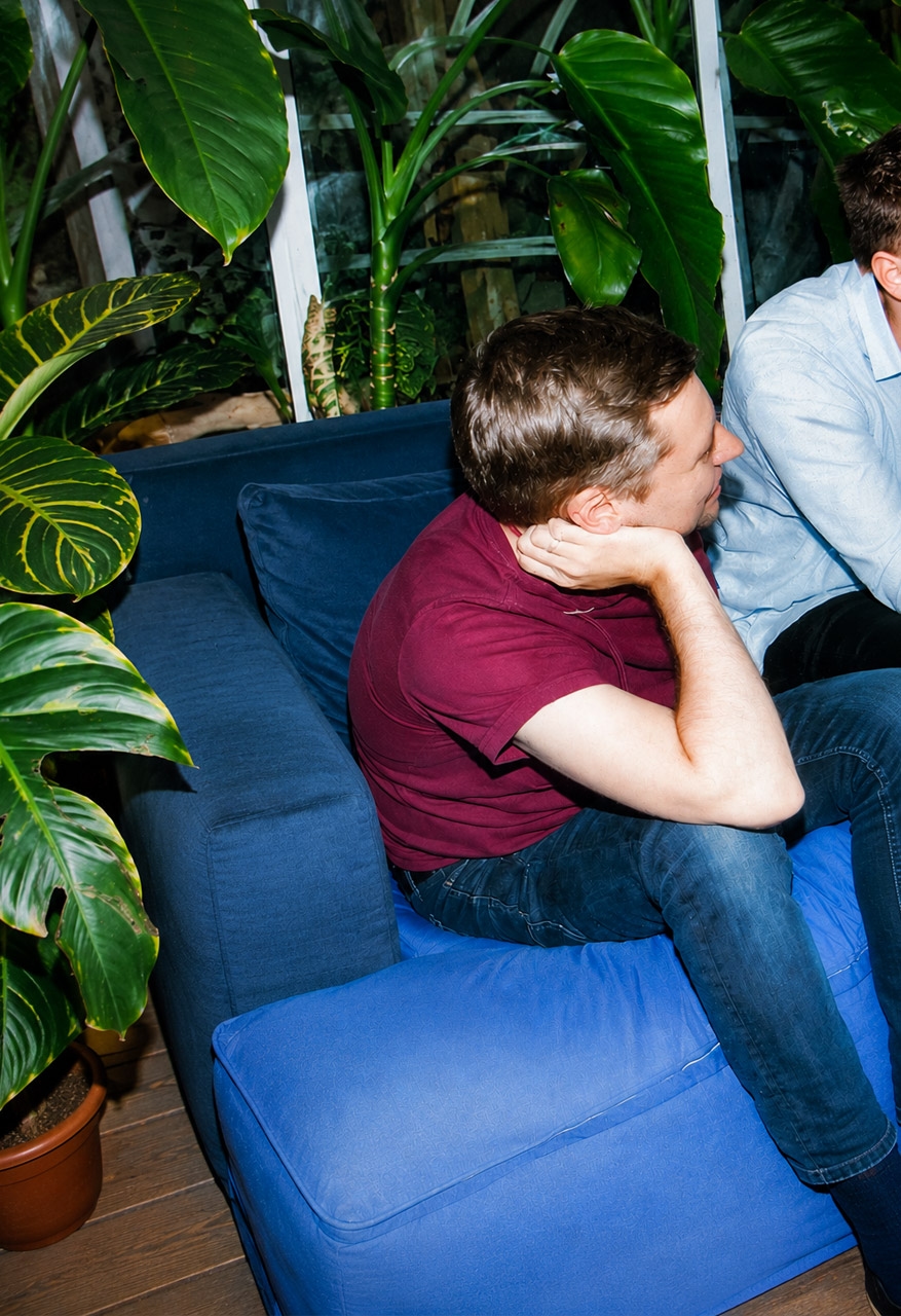 Four people are sitting relaxed on blue beanbags in a circle, surrounded by potted plants.